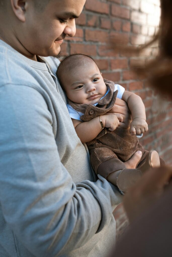 A Man in Gray Shirt Carrying a Baby Boy Wearing Brown Jumper